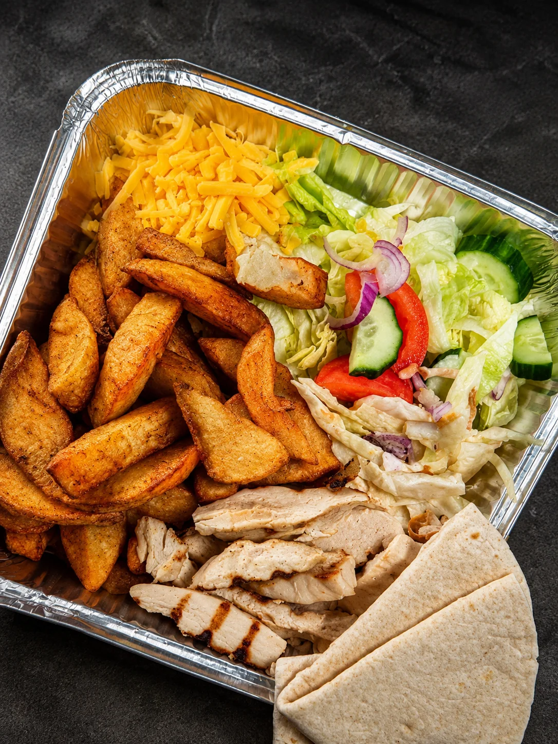 Chicken, wedges and salad with cheese in a takeaway tray